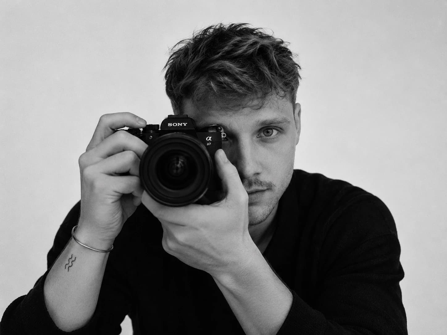 Zwart-witportret van Noah Ubert die door zijn camera recht de lens in kijkt