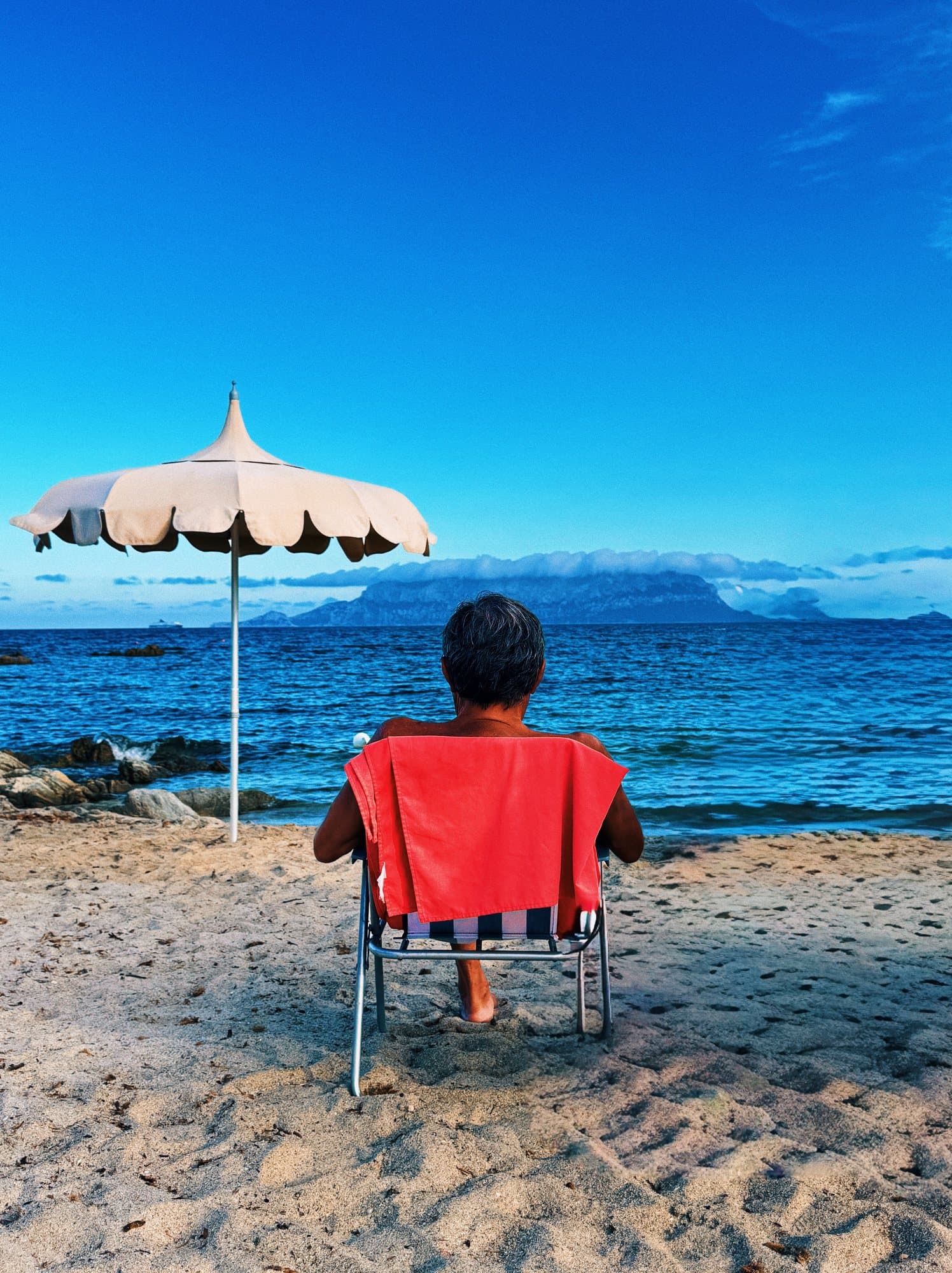Man in een strandstoel onder een parasol, uitkijkend over zee
